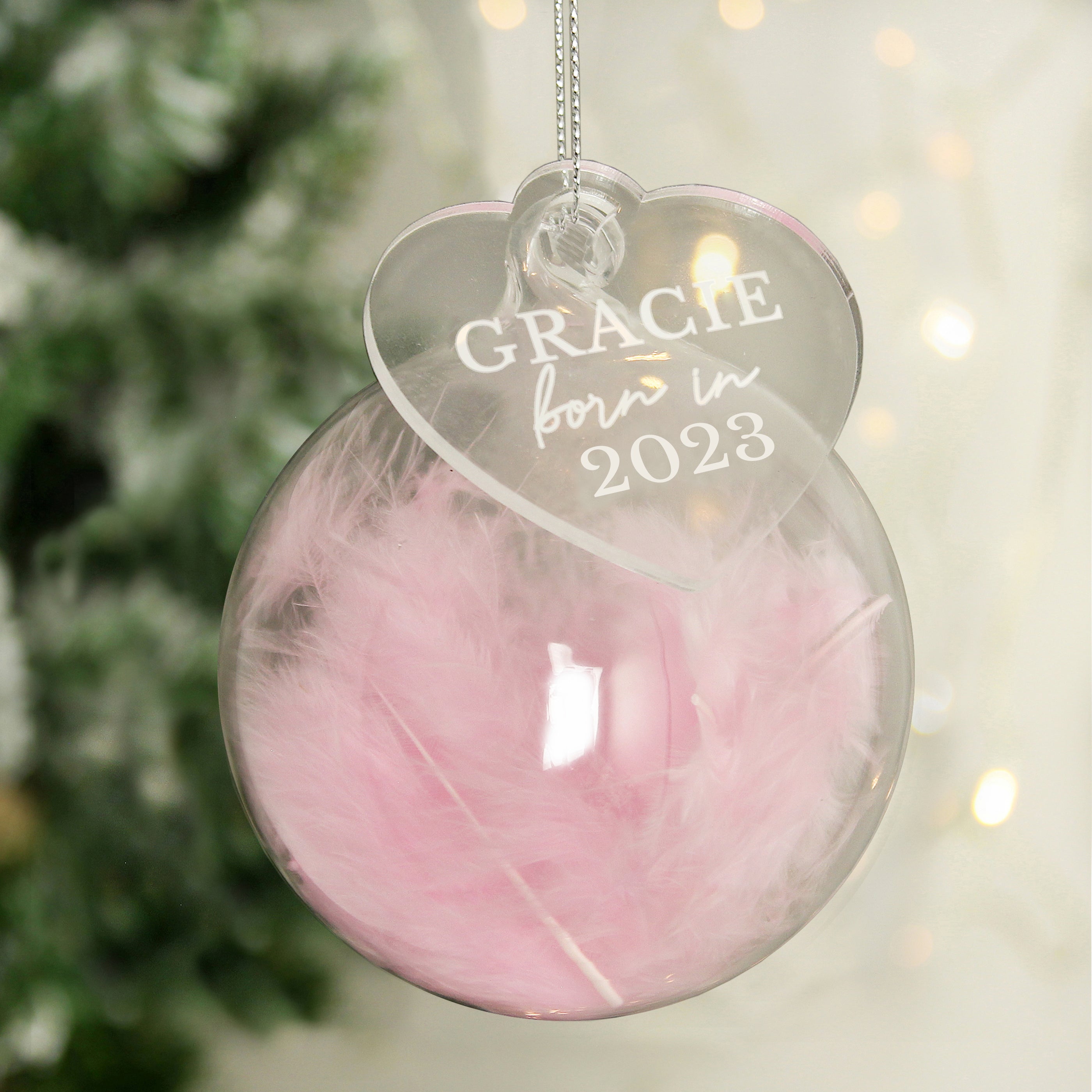 Personalised Born In Pink Feather Glass Bauble With Heart Tag Hanging From A Christmas Tree In Background