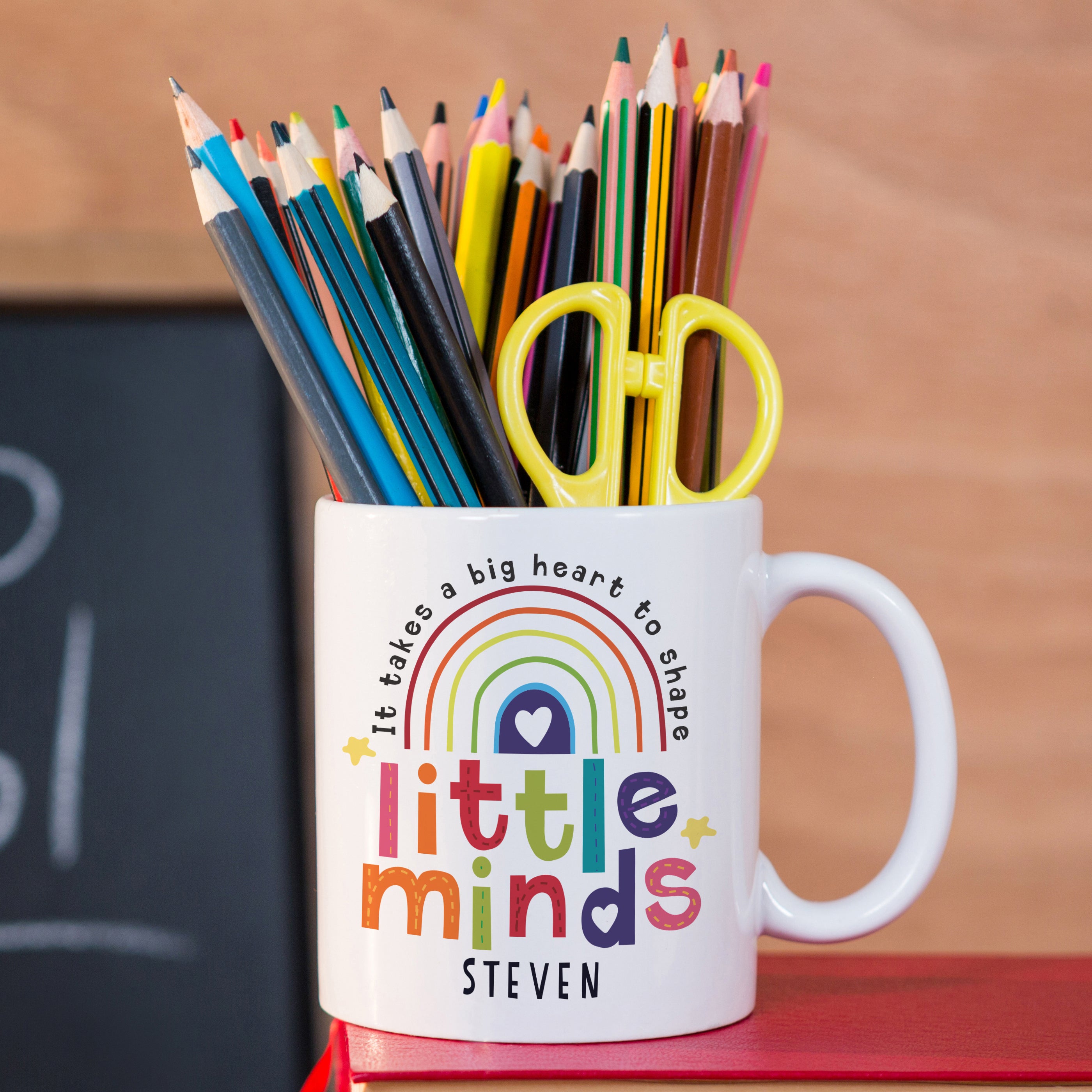 Personalised Shape Little Minds Mug Sitting On A Book Filled With Pens and Sissors